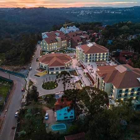 Buona Vitta Gramado Resort & Spa By Gramado Parks Bagian luar foto The photo shows an aerial view of a hotel complex set in a hilly, wooded area. The buildings feature a mix of architectural styles with several structures, including a central round pavilion. Surrounding the buildings are well-maintained gardens and 