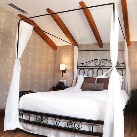 Buona Vitta Gramado Resort & Spa By Gramado Parks Bagian luar foto The photo shows a beautifully designed bedroom featuring a four-poster bed with a metal frame and flowing white curtains. The bed is adorned with white bedding and brown decorative pillows. The room has wooden beams on the ceiling and is decorated wi