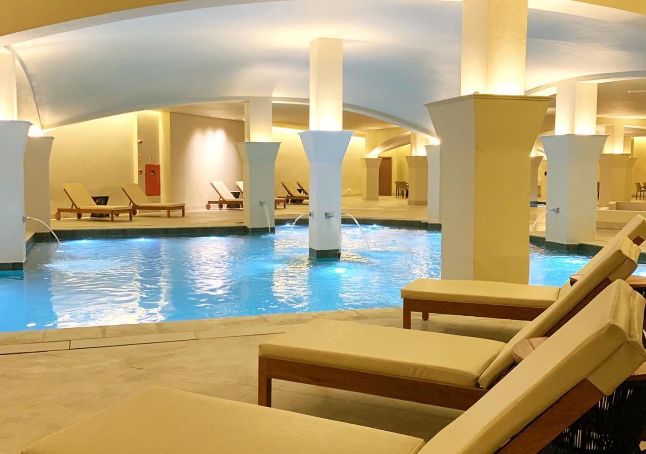 Buona Vitta Gramado Resort & Spa By Gramado Parks Bagian luar foto The photo shows an indoor spa or relaxation area with a tranquil atmosphere. There is a large swimming pool with clear blue water, illuminated by soft lighting. Surrounding the pool are several comfortable lounge chairs. The architecture features ele