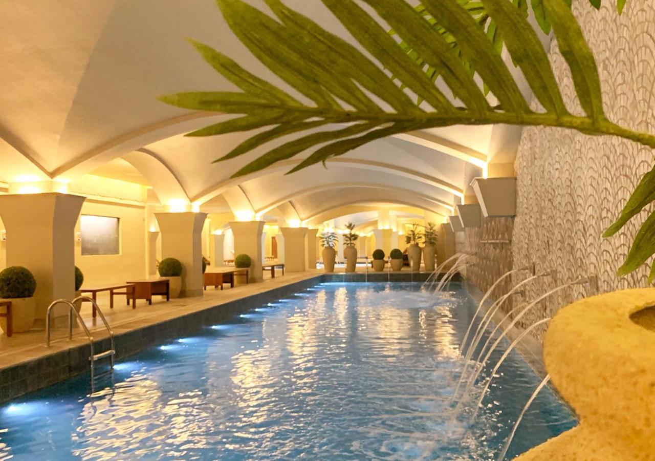 Buona Vitta Gramado Resort & Spa By Gramado Parks Bagian luar foto The photo shows an indoor swimming pool with a serene and elegant atmosphere. The pool has a calm blue water surface, illuminated by soft lights along its edges. The architectural design features arches in the ceiling, creating an open and spacious f