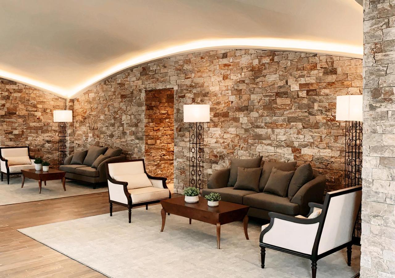 Buona Vitta Gramado Resort & Spa By Gramado Parks Bagian luar foto The photo shows a stylish and modern lounge area. The walls are made of natural stone, creating a warm and inviting atmosphere. There are two comfortable sofas in a muted gray color arranged around a wooden coffee table. Flanking the sofas are elegan