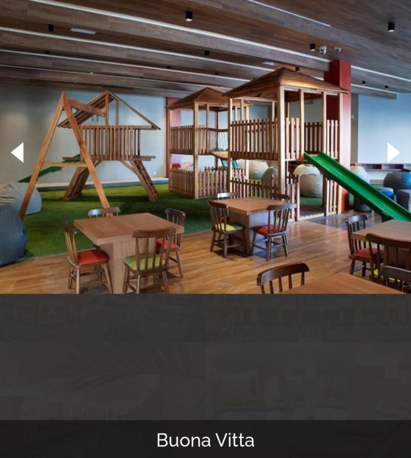 Buona Vitta Gramado Resort & Spa By Gramado Parks Bagian luar foto The photo shows a play area designed for children, featuring a wooden play structure with slides and climbing areas. In the foreground, there are several small wooden tables and chairs arranged for seating. The floor is covered with green turf, resem