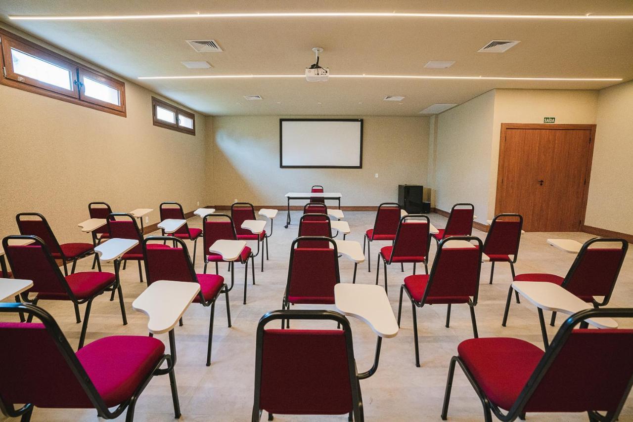 Buona Vitta Gramado Resort & Spa By Gramado Parks Bagian luar foto The photo shows a classroom or meeting room set up for a presentation or lecture. It features several rows of red chairs, each with a small writing surface attached. There is a blank screen mounted on the wall at the front of the room, likely for dis