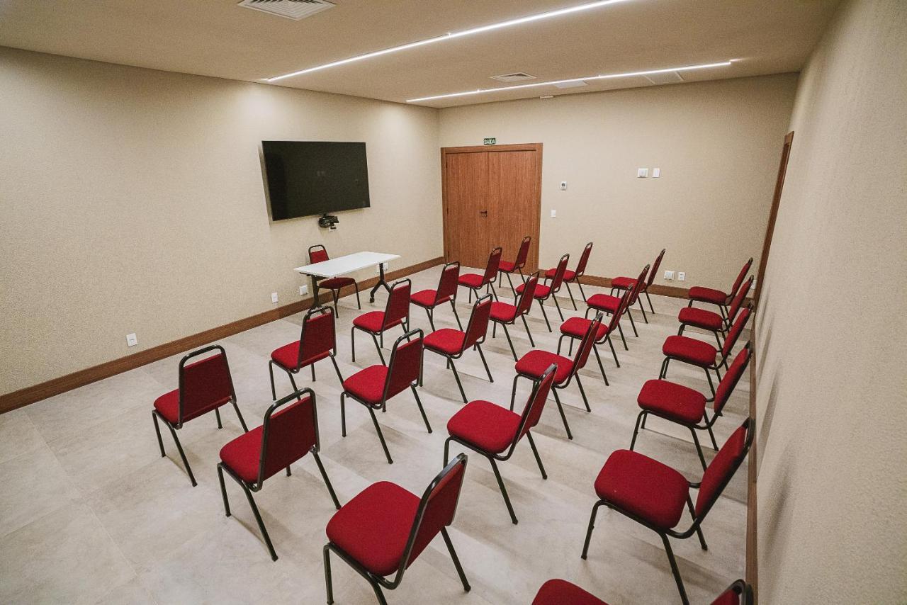 Buona Vitta Gramado Resort & Spa By Gramado Parks Bagian luar foto The photo shows a conference or meeting room with a simple and modern design. There are several rows of red chairs arranged in a semi-circle facing a white table at the front. On the wall opposite the chairs, there is a flat-screen television mounted