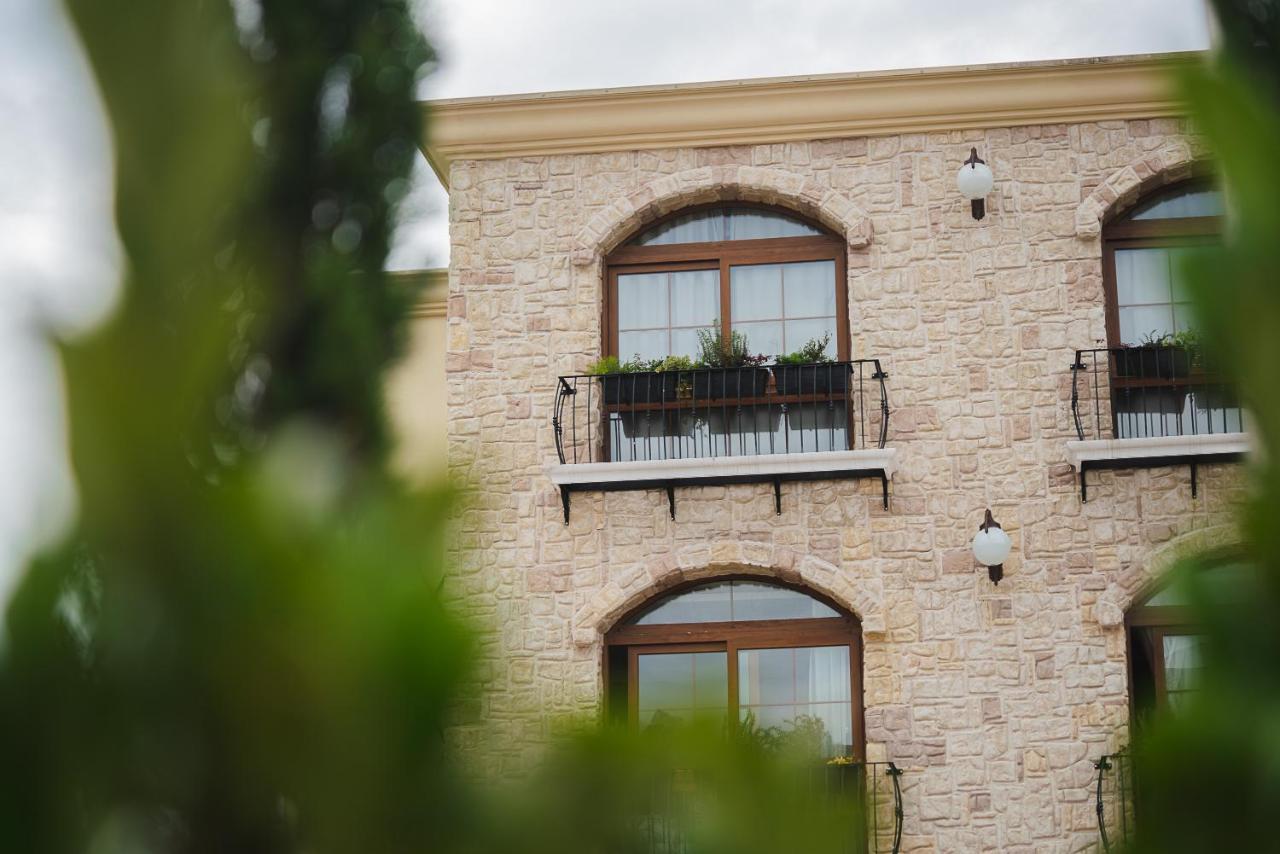 Buona Vitta Gramado Resort & Spa By Gramado Parks Bagian luar foto The photo depicts a stone building with a textured exterior. It features several windows with wooden frames. Each window has a small balcony adorned with decorative plants. There are also wall-mounted light fixtures flanking the windows. In the foreg