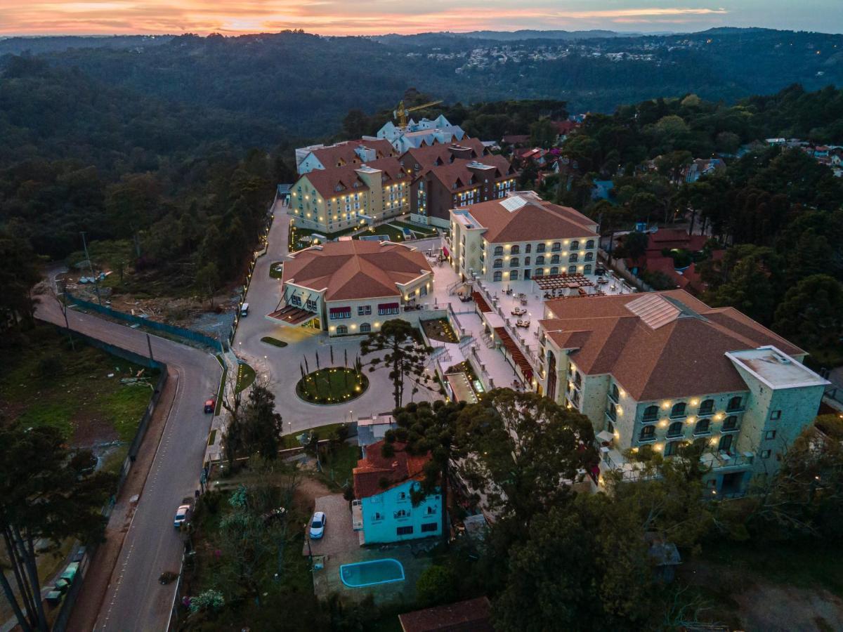 Buona Vitta Gramado Resort & Spa By Gramado Parks Bagian luar foto The photo shows an aerial view of a hotel complex set in a hilly, wooded area. The buildings feature a mix of architectural styles with several structures, including a central round pavilion. Surrounding the buildings are well-maintained gardens and 