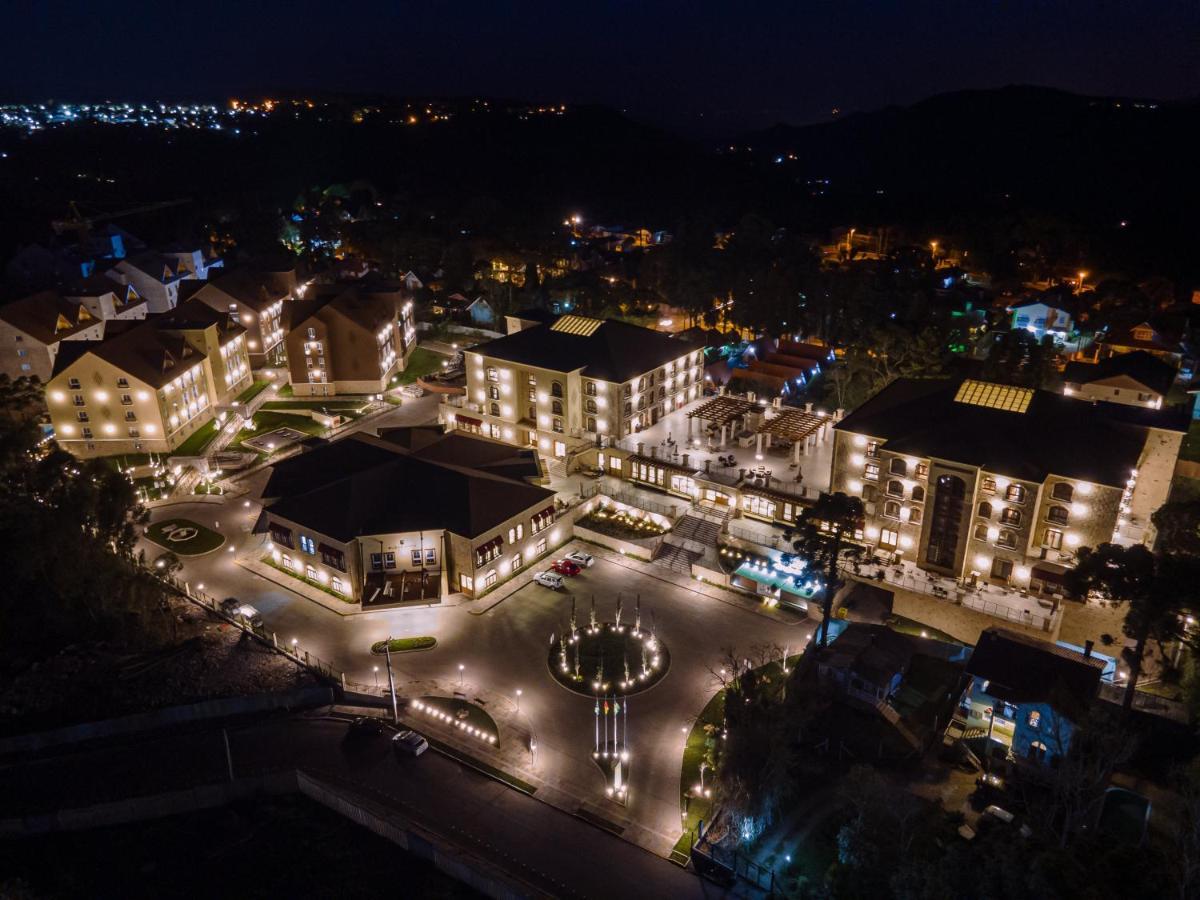 Buona Vitta Gramado Resort & Spa By Gramado Parks Bagian luar foto The photo shows a beautifully lit resort or hotel complex taken at night. The buildings are well-illuminated, highlighting their architecture. There is a circular area with a fountain at the center, surrounded by pathways that connect various parts o