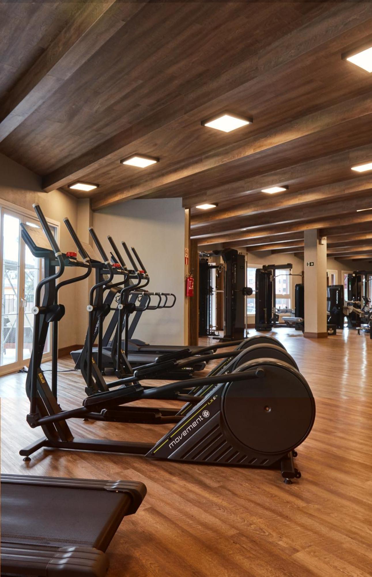 Buona Vitta Gramado Resort & Spa By Gramado Parks Bagian luar foto The photo shows a modern gym interior with wooden flooring and a ceiling with wooden beams. There are several exercise machines, including elliptical trainers and a treadmill, positioned in the foreground. In the background, there are additional work