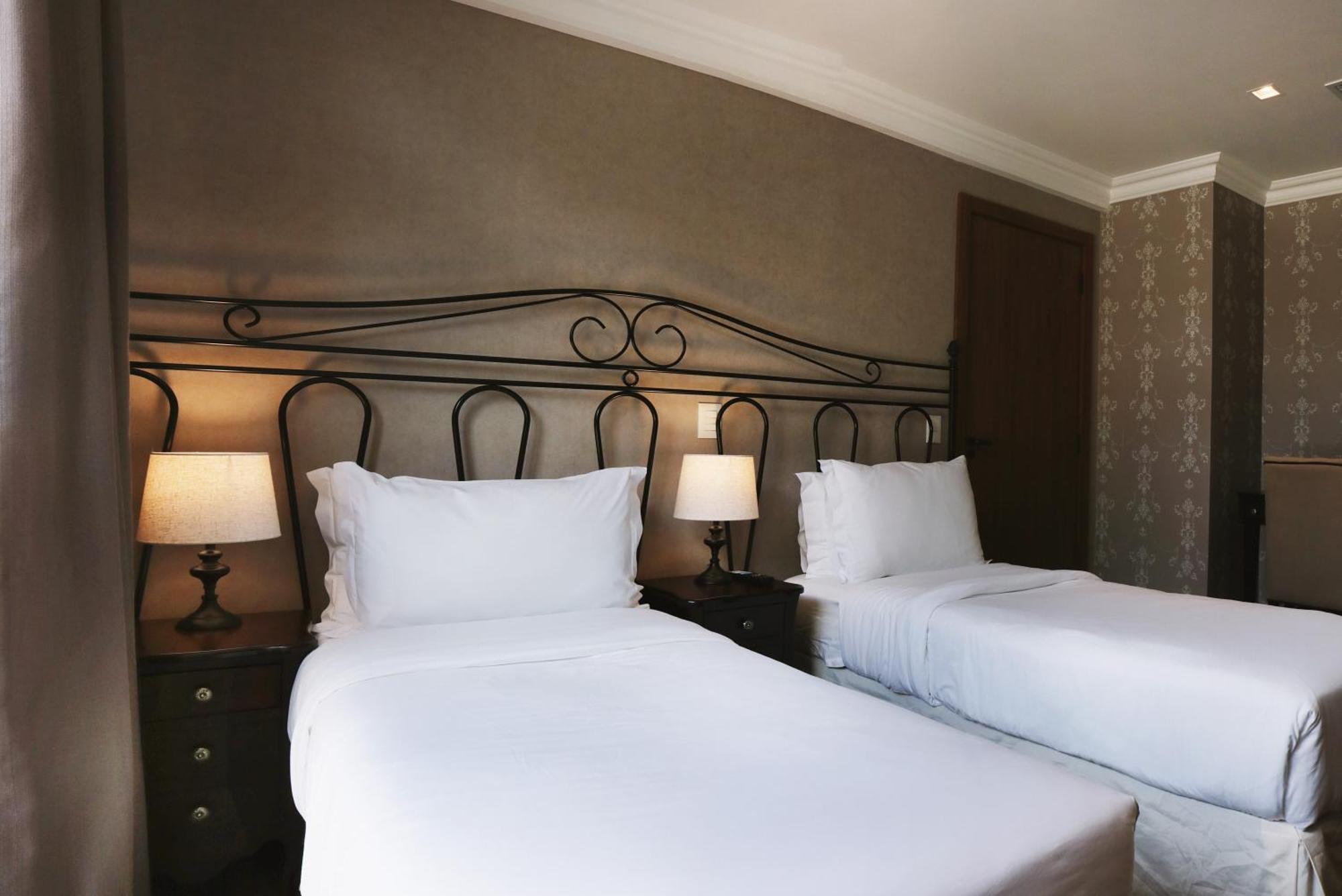 Buona Vitta Gramado Resort & Spa By Gramado Parks Bagian luar foto The photo shows a neatly arranged hotel room featuring two single beds with white bedding. The beds have decorative metal headboards, and there are bedside tables on either side with lamps. The room's walls have a subtle design, and there is a door v