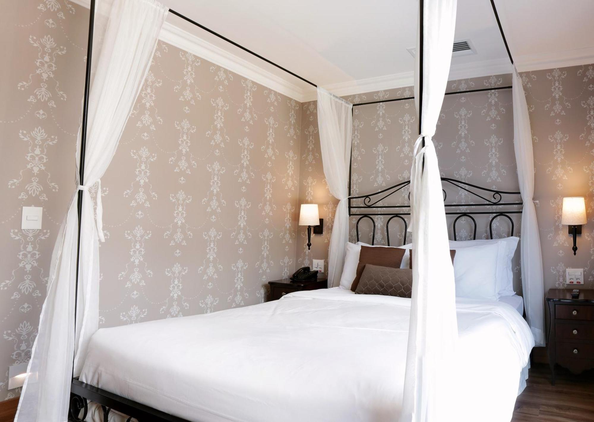 Buona Vitta Gramado Resort & Spa By Gramado Parks Bagian luar foto The photo shows a elegantly decorated bedroom featuring a four-poster bed with white drapes. The bed is made with white linens and has some brown accent pillows. The walls are adorned with a subtle floral pattern, and there are two bedside lamps prov
