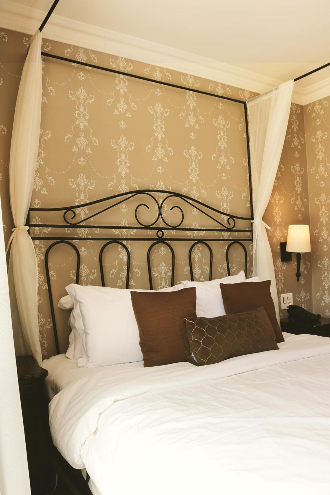 Buona Vitta Gramado Resort & Spa By Gramado Parks Bagian luar foto The photo shows a cozy bedroom setup featuring a decorative metal bed frame with a scroll design as the headboard. The bed is adorned with several white pillows and two brown decorative cushions. The wall behind the bed is covered with a light-colore