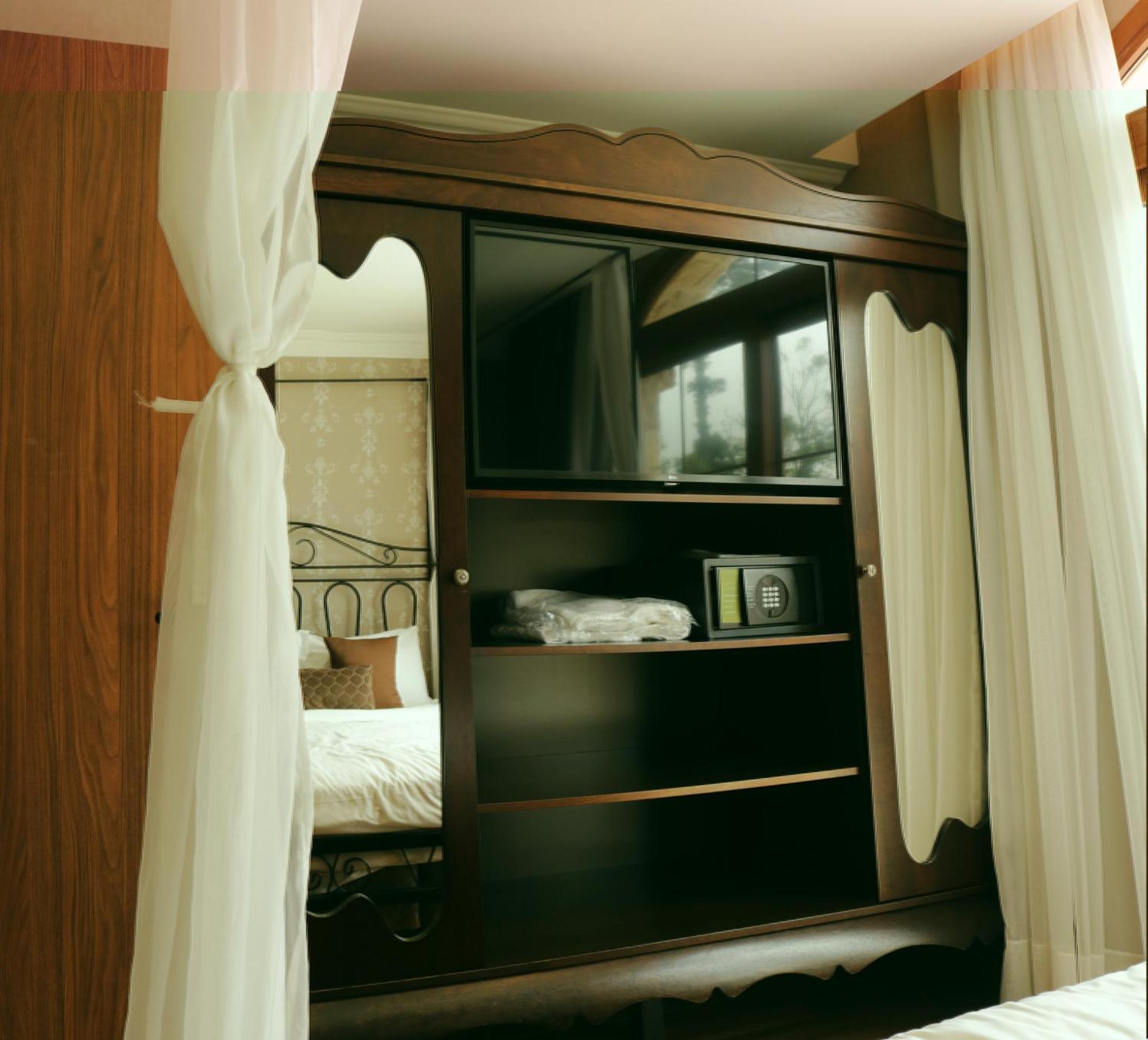 Buona Vitta Gramado Resort & Spa By Gramado Parks Bagian luar foto The image shows a wooden cabinet with a television mounted on the front. The cabinet has decorative edges and is paired with sheer white curtains on either side. Inside the cabinet, there are shelves, and a small safe or storage box is visible on one