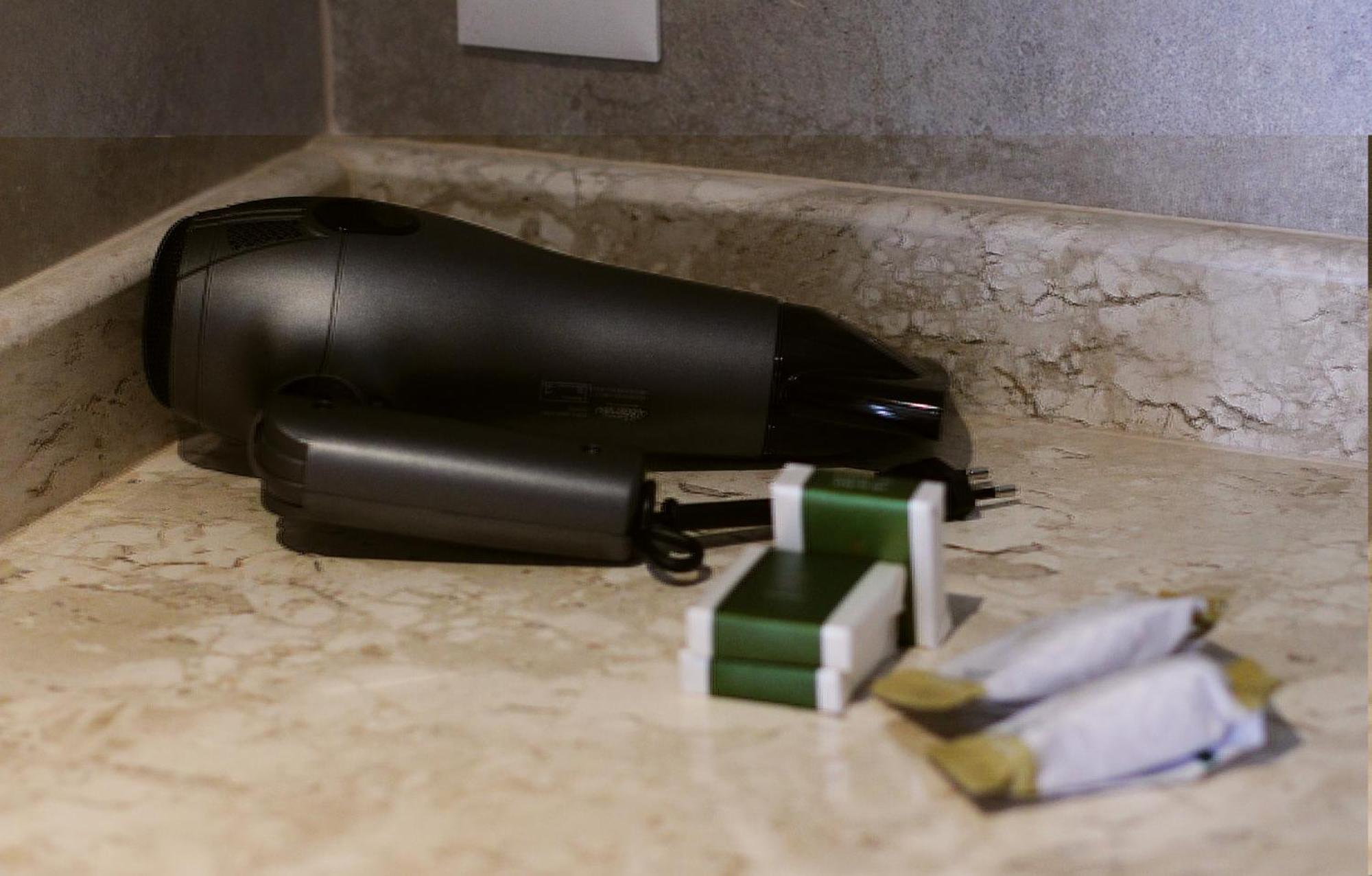 Buona Vitta Gramado Resort & Spa By Gramado Parks Bagian luar foto The photo shows a black hairdryer placed on a marble countertop. Next to the hairdryer, there are two wrapped items, likely toiletries, with green and white packaging. Additionally, there are two more items, also wrapped, which appear to be in simila