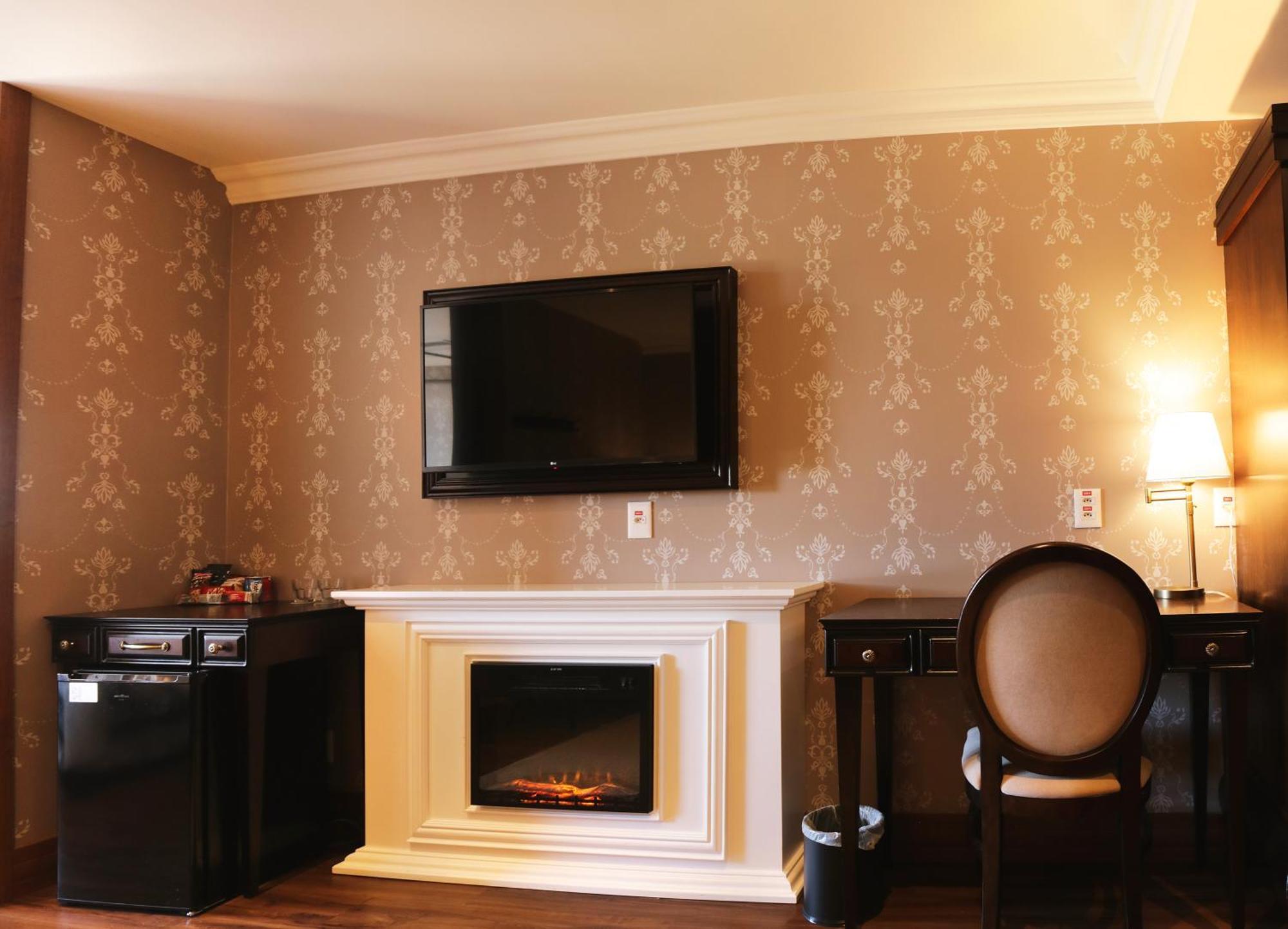 Buona Vitta Gramado Resort & Spa By Gramado Parks Bagian luar foto The photo shows a cozy room featuring a decorative wall with a subtle pattern. On one side, there is a modern flat-screen television mounted on the wall. Below it, there is a stylish electric fireplace framed in white. Adjacent to the fireplace is a 