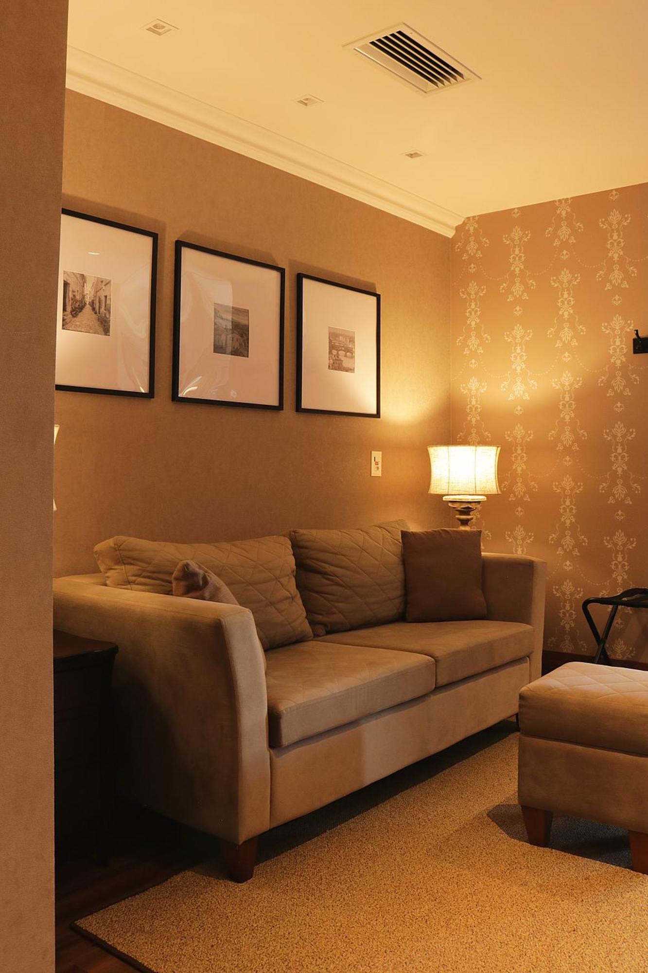 Buona Vitta Gramado Resort & Spa By Gramado Parks Bagian luar foto The photo shows a cozy living room setting. There is a light-colored sofa adorned with several cushions, positioned against a wall that has a subtle pattern. Above the sofa, there are three framed artworks or photographs hanging on the wall. To the s