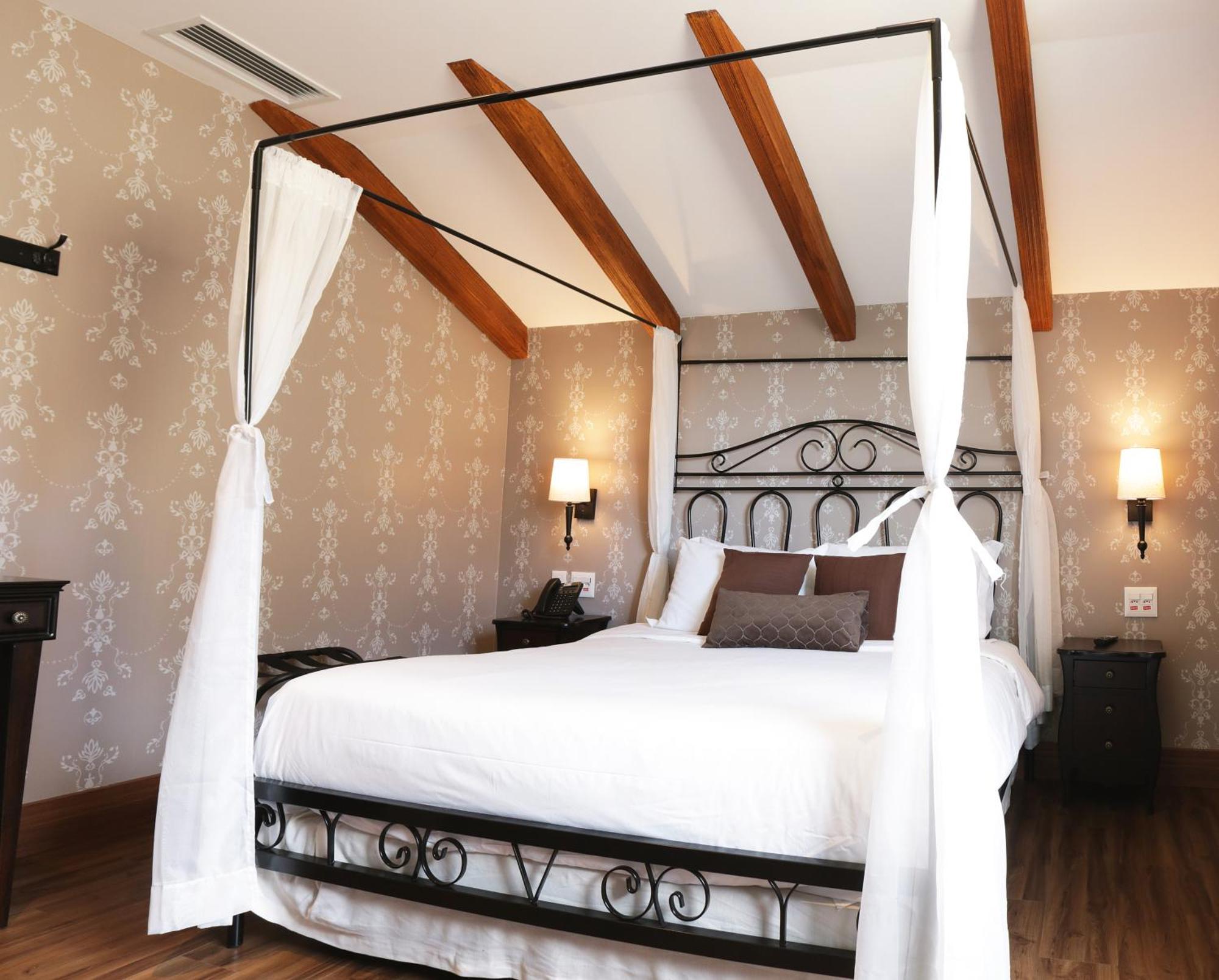 Buona Vitta Gramado Resort & Spa By Gramado Parks Bagian luar foto The photo shows a beautifully designed bedroom featuring a four-poster bed with a metal frame and flowing white curtains. The bed is adorned with white bedding and brown decorative pillows. The room has wooden beams on the ceiling and is decorated wi