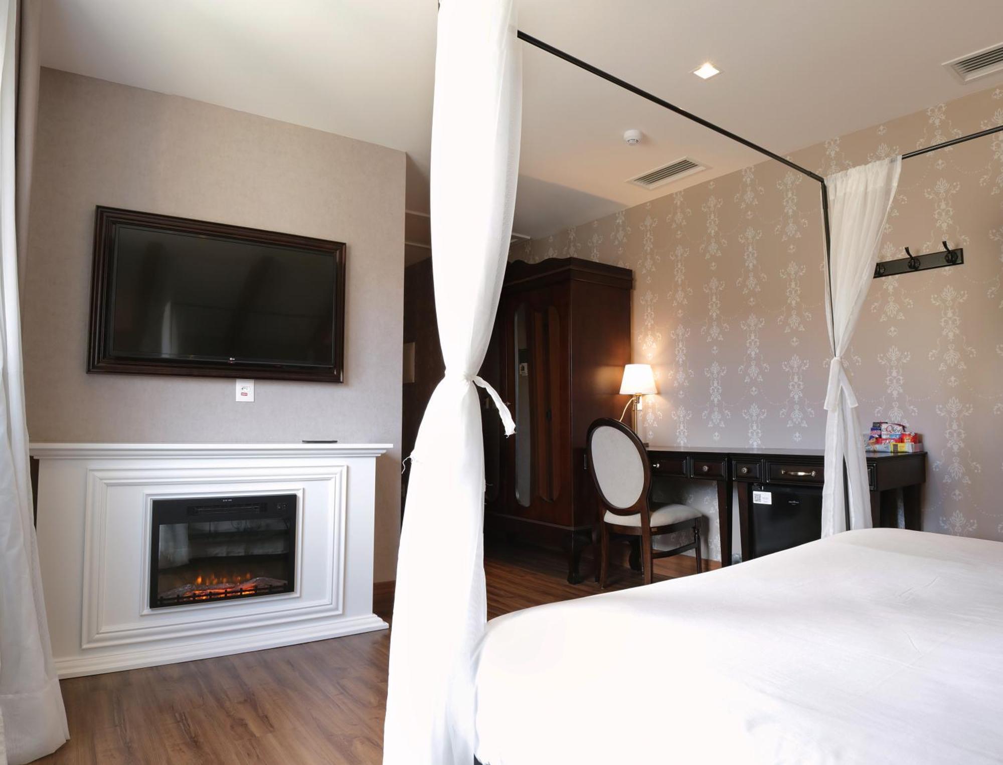 Buona Vitta Gramado Resort & Spa By Gramado Parks Bagian luar foto The photo shows a cozy hotel room with elegant decor. There is a white bed with a canopy, and a modern television mounted on the wall across from it. To the side, a fireplace is built into a white mantel, adding a warm touch to the space. There's a w