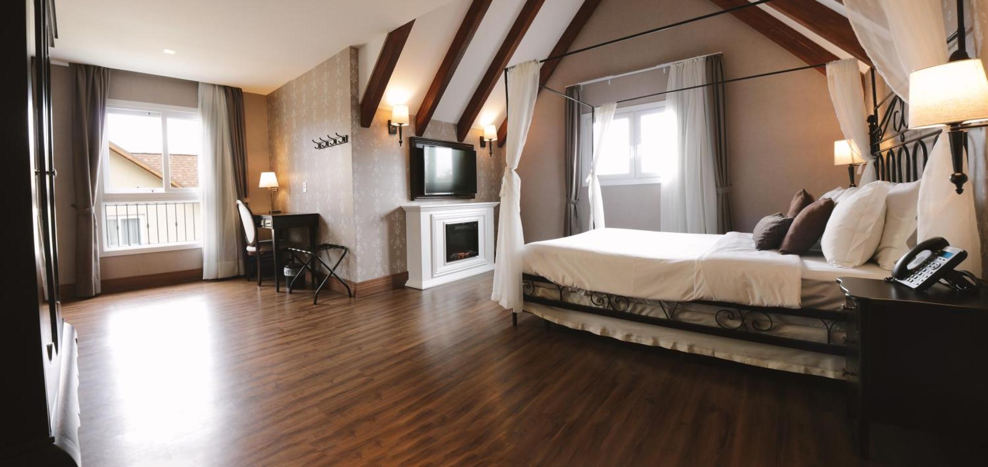 Buona Vitta Gramado Resort & Spa By Gramado Parks Bagian luar foto The photo shows a spacious hotel room with a modern and elegant design. There is a large bed with an overhead canopy, and the bed is dressed in white linens. To the side, there is a small seating area with a desk and chair. A flat-screen television i