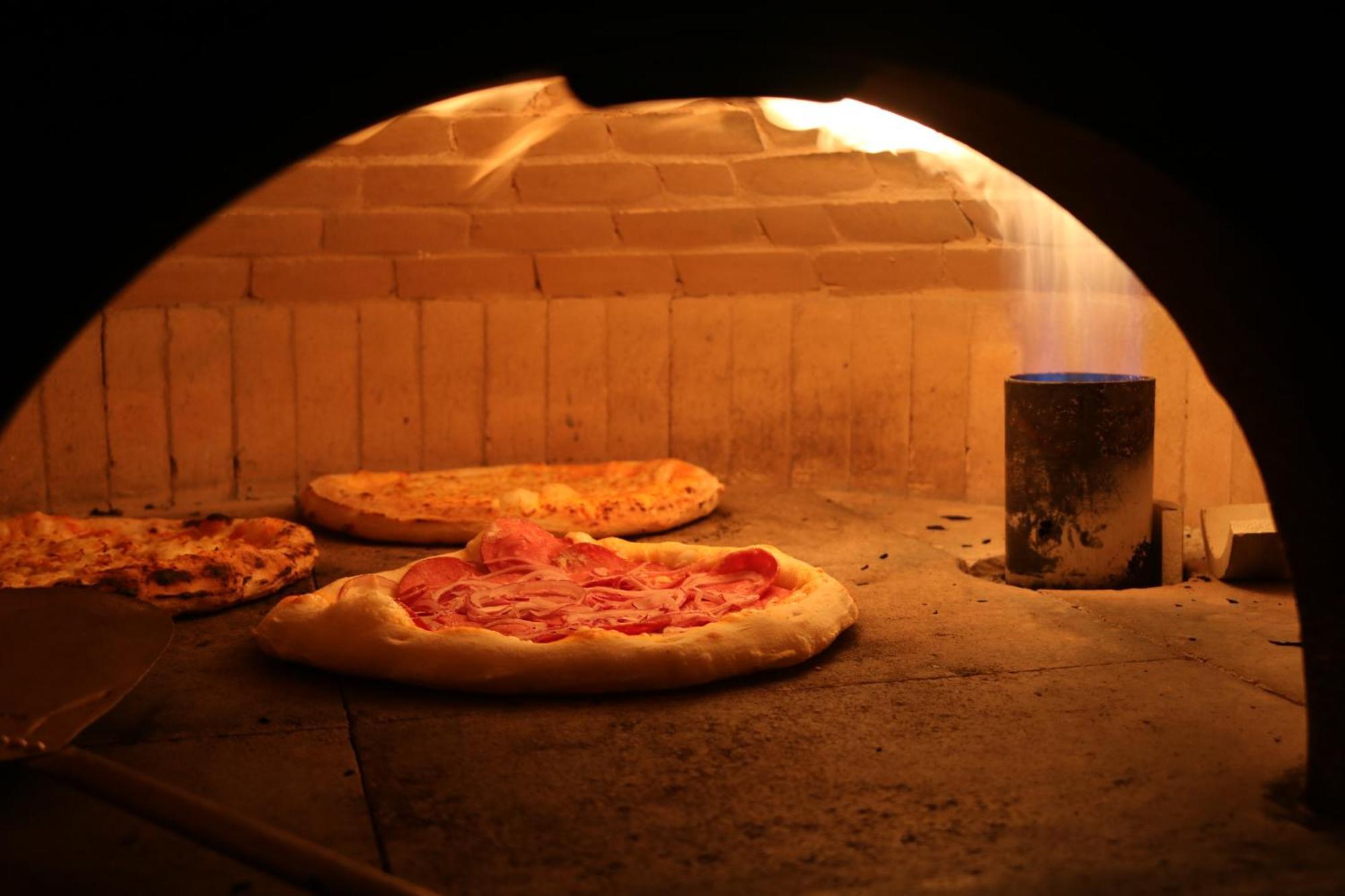 Buona Vitta Gramado Resort & Spa By Gramado Parks Bagian luar foto The photo shows a traditional pizza oven. Inside the oven, there are several pizzas placed on the stone surface. The pizzas appear to have various toppings, including what looks like cheese and possibly pepperoni. The oven has a warm, glowing ambianc